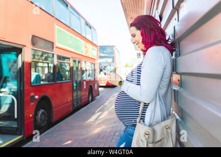 Femme enceinte en utilisant son téléphone à l'arrêt de bus Banque D'Images