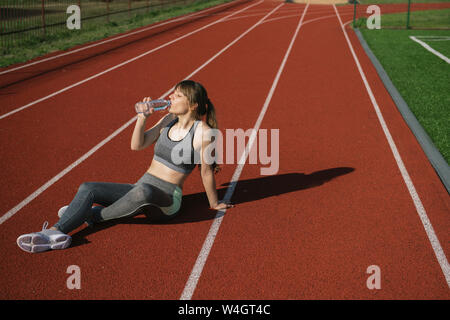 Grande sportive assis sur racetrack et l'eau potable après entraînement Banque D'Images