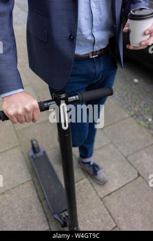 Businessman with E-scooter et le café d'aller marcher sur la chaussée, vue partielle Banque D'Images