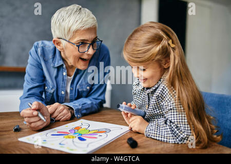 Grand-mère et petite-fille assis à table, livre de coloriage peinture Banque D'Images