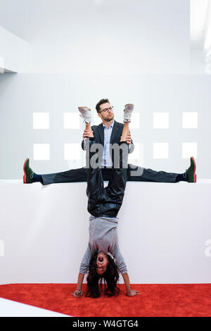 Businessman in office holding woman's legs faire un handstand Banque D'Images