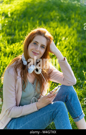 Jeune femme rousse au casque et le smartphone dans un parc Banque D'Images