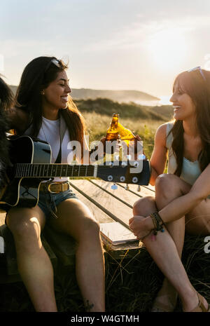 Deux femmes heureux avec guitare cliquetis des bouteilles de bière dans des dunes boardwalk Banque D'Images