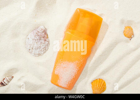 Bouteille d'orange de l'écran solaire sur le sable avec les coquillages Banque D'Images