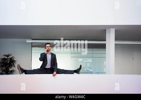 Businessman doing the splits sur réception dans office talking on cell phone Banque D'Images