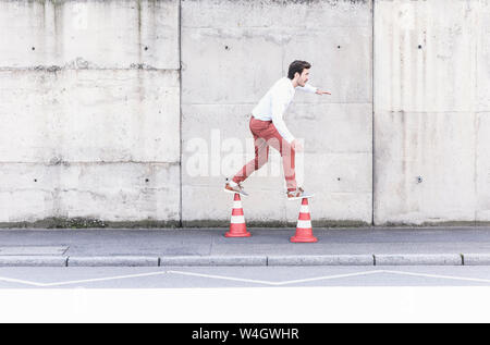 Jeune homme en équilibre sur cônes de circulation en face de mur de béton Banque D'Images