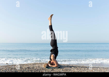 Young woman practicing yoga sur la plage, faire la tête Banque D'Images