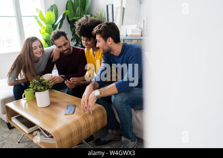 Quatre happy friends sitting on couch using cell phone Banque D'Images