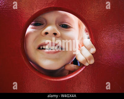 Portrait of smiling little boy à la recherche à travers le trou à l'aire de jeux Banque D'Images