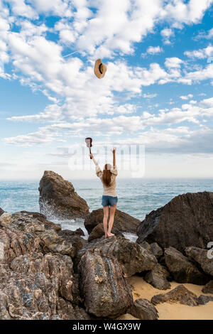 Vue arrière de jeune femme avec ukulele debout sur rock hat jeter en l'air Banque D'Images