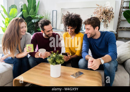 Quatre happy friends sitting on couch using cell phone Banque D'Images