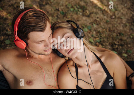 Jeune couple lying on grass, écouter de la musique avec des écouteurs Banque D'Images