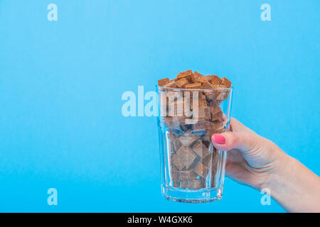 Vue partielle de la femelle avec le verre plein de cubes de sucre brun sur bleu isolé Banque D'Images