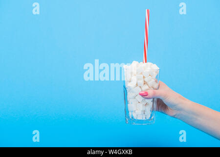 Vue partielle de woman holding glass avec de la paille et de cubes de sucre blanc sur bleu isolé Banque D'Images