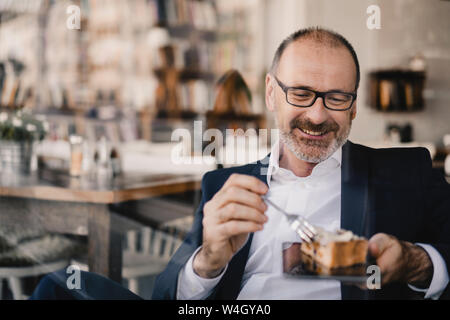 Homme d'âge mûr ayant un morceau de gâteau sur une tablette numérique dans un café Banque D'Images