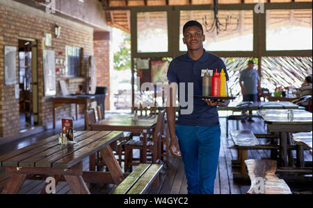 Young waiter serving sauces dans bouteilles dans un restaurant, Afrique du Sud Banque D'Images