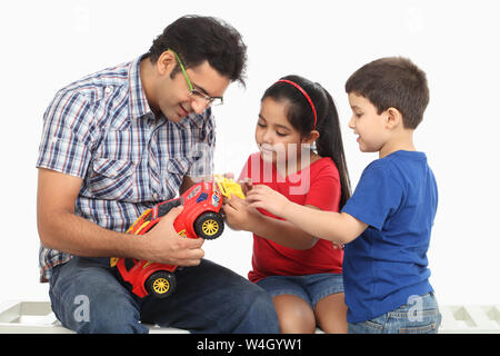 Homme avec ses enfants réparant une voiture-jouet Banque D'Images