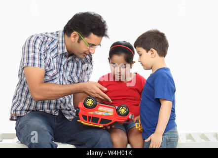 Homme avec ses enfants réparant une voiture-jouet Banque D'Images