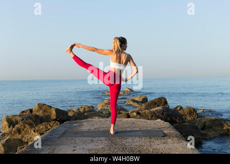 Young woman practicing yoga sur la plage, faisant de l'équilibre, Utthita Hasta Padangustasana Banque D'Images