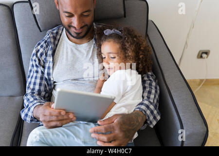 Père et fille assis sur table à la maison ensemble, à la tablette à Banque D'Images