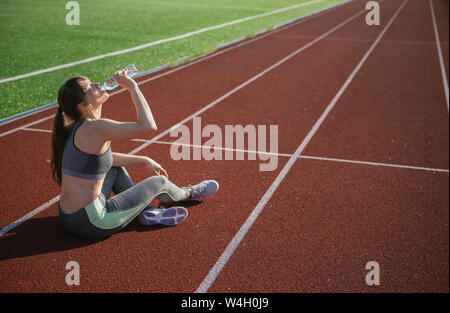 Grande sportive assis sur racetrack et l'eau potable après entraînement Banque D'Images