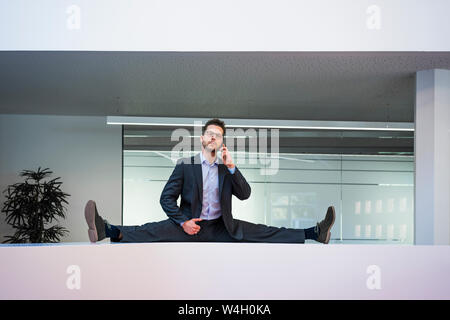 Businessman doing the splits sur réception dans office talking on cell phone Banque D'Images