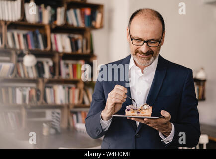 Homme d'âge mûr ayant un morceau de gâteau sur une tablette numérique dans un café Banque D'Images