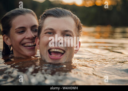 Jeune couple nager dans le lac au coucher du soleil Banque D'Images