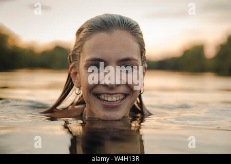 Jeune femme natation dans le lac au coucher du soleil Banque D'Images