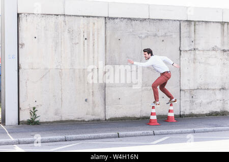 Jeune homme en équilibre sur cônes de circulation en face de mur de béton Banque D'Images