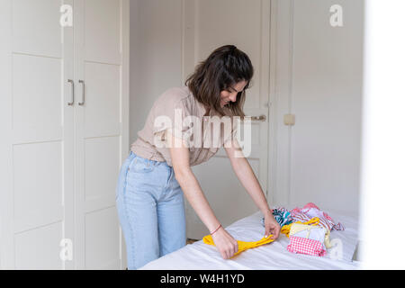 Jeune femme mise sur le lit vêtements Banque D'Images