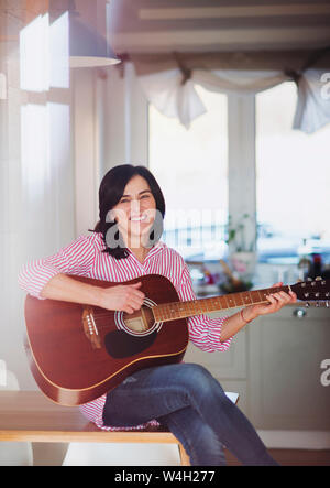 Portrait of smiling mature woman playing guitar at home Banque D'Images