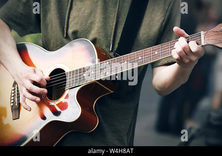 Un jeune garçon arrogant dans une capuche verte joue un acoustique de couleur vive guitare à six cordes, tenant les cordes d'une main et tenant un médiateur dans le Banque D'Images