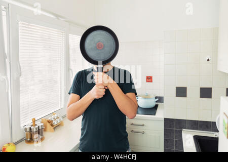 Un jeune homme porte sur son visage avec une poêle. Photo prise à la cuisine. Banque D'Images