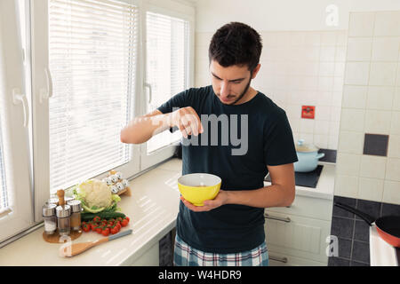 Jeune homme séduisant est le petit-déjeuner dans la cuisine à la maison. Le gars s'est préparé d'avoine et d'un verre de lait pour le petit-déjeuner. Banque D'Images