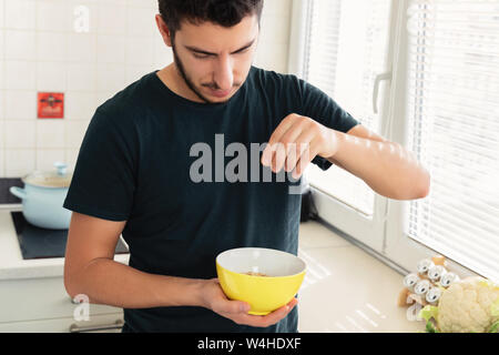 Jeune homme séduisant est le petit-déjeuner dans la cuisine à la maison. Le gars s'est préparé d'avoine et d'un verre de lait pour le petit-déjeuner. Banque D'Images