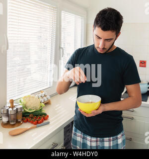 Jeune homme séduisant est le petit-déjeuner dans la cuisine à la maison. Le gars s'est préparé d'avoine et d'un verre de lait pour le petit-déjeuner. Banque D'Images