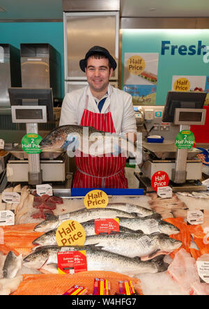 Poissonnier mâle tenant un grand poisson sur le poisson frais affichage à une succursale de Tesco Banque D'Images