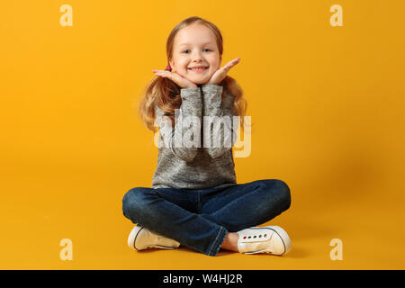 Portrait d'une belle jolie belle charmante petite fille joyeuse. L'enfant est assis sur un fond jaune dans le studio. Banque D'Images