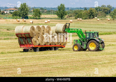 Tracteur tour de chargement des balles de foin sur la remorque pour transport à destination dans la campagne toscane, italie Banque D'Images