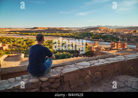 Un touriste garçon assis et regarder le coucher du soleil dans la vallée sous l'ancienne ville historique de Ait Ben Haddou en Afrique Maroc Banque D'Images