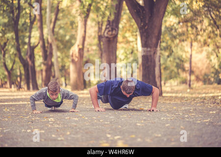 Petit garçon et son père faire des pousées exercices ensemble dans le parc. Père et fils passent du temps ensemble et de mener une vie saine.Working Out Banque D'Images