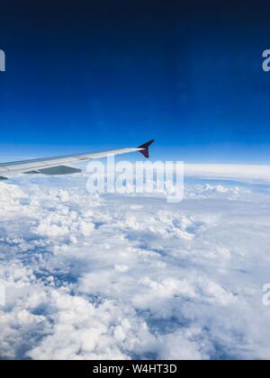 Vue hors de la fenêtre de l'avion montrant l'extrémité d'une aile d'avion sur des nuages blancs denses et un fond bleu clair de ciel. Banque D'Images