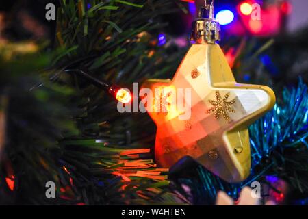 Ornement en forme d'étoile dorée suspendu sur un arbre de Noël, illuminé par une lumière rouge brillante. Décor de Noël authentique dans une maison familiale. Banque D'Images