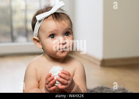 Le bébé est assis sur le sol dans la couche et mange des guimauves. N'est pas interdit à un bon repas. Banque D'Images