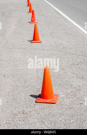 Rangée de cônes de signalisation orange en perspective parallèle à la ligne blanche sur l'asphalte. Banque D'Images