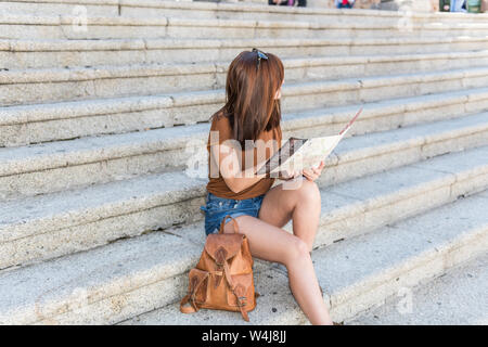 Rousse jeune touriste avec un sac à dos consulte un site sur les marches de la place principale de Cáceres Banque D'Images