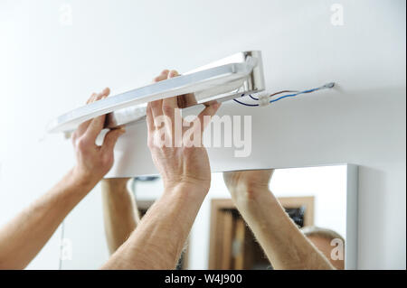 L'installation d'une lampe à la maison. L'homme est de fixer la lampe sur le mur au-dessus du miroir. Banque D'Images