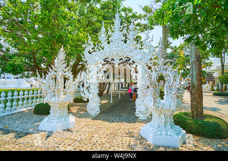 CHIANG RAI, THAÏLANDE - Mai 9, 2019 : La porte richement décorée à l'entrée de la ruelle couverte (toit) du Temple blanc, entouré par des greener Banque D'Images