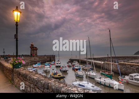 Lynmouth Harbour, North Devon, Angleterre. Le mardi 23 juillet 2019. Météo britannique. Au crépuscule, les lampadaires de scintillement sur dans le petit port pittoresque de Lynmouth comme la prévision des tempêtes orageuses l'approche de la côte nord du Devon. Credit : Terry Mathews/Alamy Live News Banque D'Images